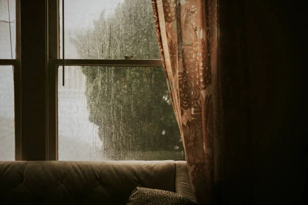 Rain running down an old window beside a heavy patterned curtain